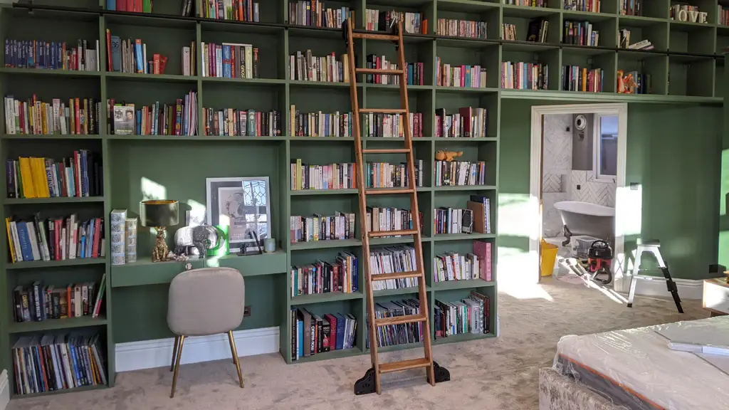 A stunning home library with floor-to-ceiling green bookshelves, a wooden rolling ladder, and a cozy reading nook with a built-in desk.
