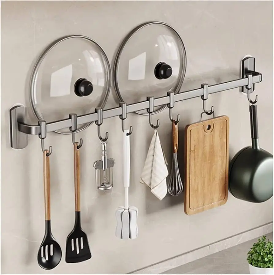 A sleek stainless steel wall-mounted kitchen rack with hooks for hanging utensils, a cutting board, a frying pan, and a built-in holder for pot lids.