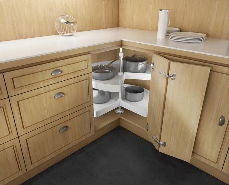 A modern corner kitchen cabinet with a rotating lazy Susan shelf system, neatly storing stainless steel pots and pans.