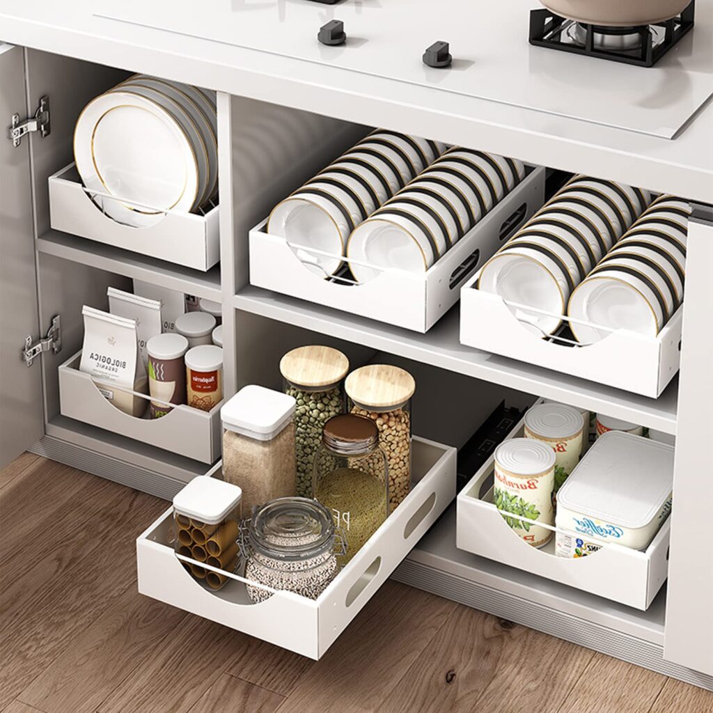 A neatly organized kitchen cabinet with white pull-out storage trays holding plates, pantry essentials, glass jars, and canned goods.