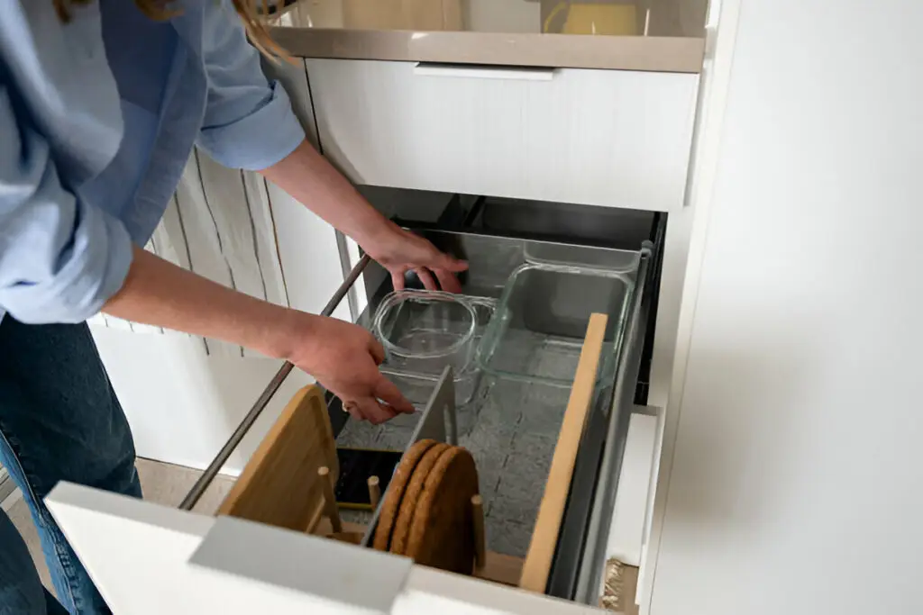 10 Eco-Friendly Kitchen Cabinet Storage Ideas for a Greener Home 9 Person organizing kitchen drawer with glass containers