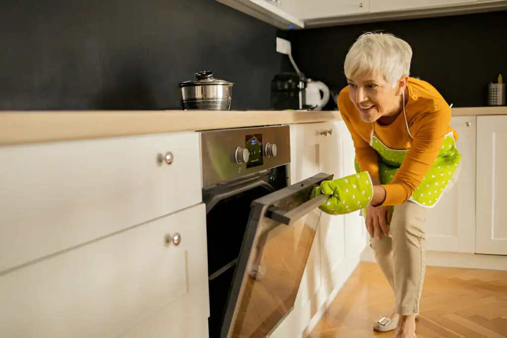 10 Eco-Friendly Kitchen Cabinet Storage Ideas for a Greener Home 14 Senior woman using oven in modern kitchen.