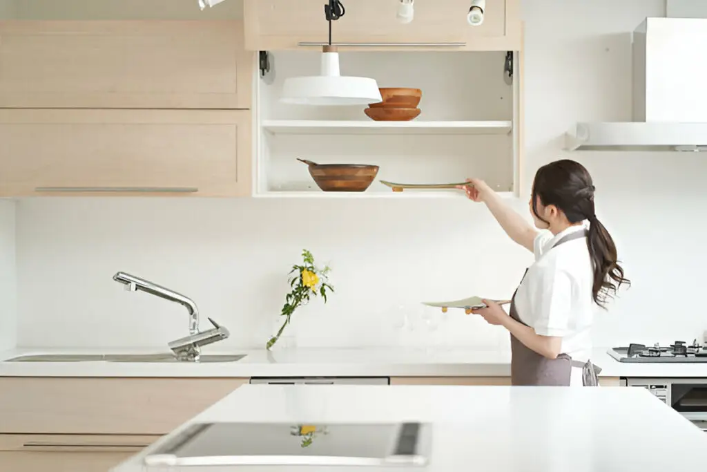 How to Organize Your Kitchen Cabinets Like a Pro (Step-by-Step Guide) 3 Modern kitchen with light wood cabinets, a woman organizing dishes, and a clean minimalist design