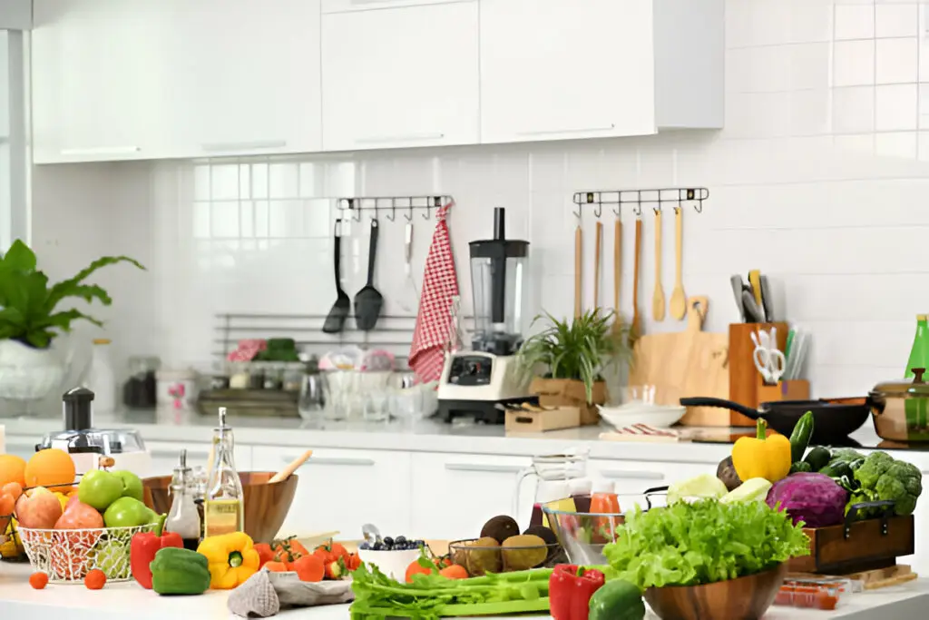 10 Must-Have Kitchen Cabinet Accessories for a Super Organized Space 4 A bright and modern kitchen with fresh vegetables, fruits, and kitchen utensils neatly arranged on a white countertop, featuring a blender, wooden spoons, and a well-organized cooking space.