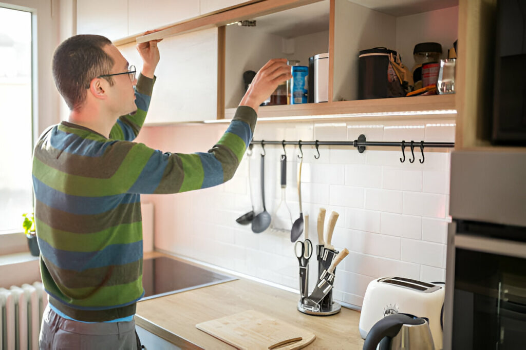Hidden Kitchen Cabinet Storage Ideas You Need to Try 1 A man organizing items in upper kitchen cabinets in a modern kitchen