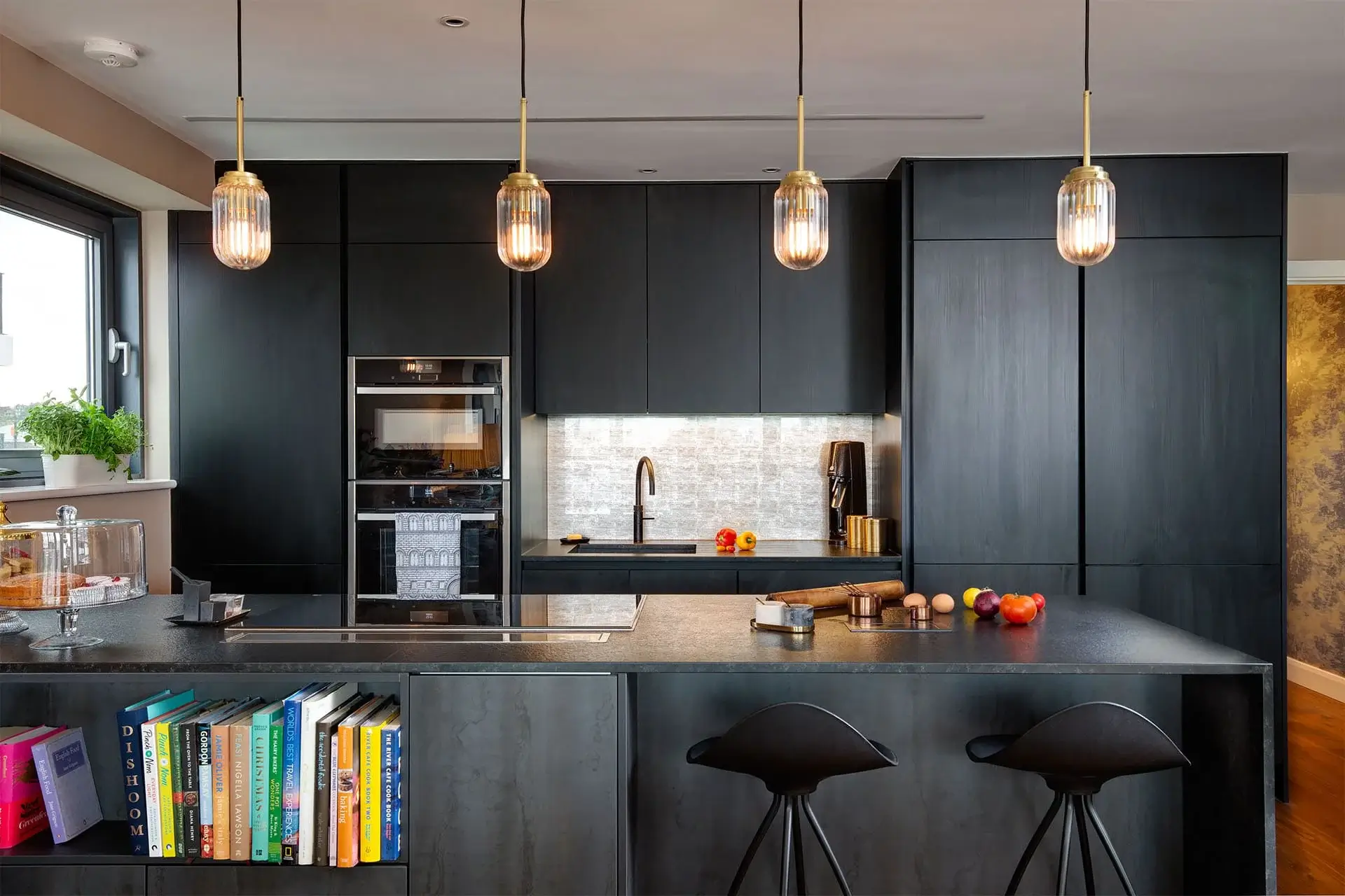 Contemporary matte black kitchen with a central island, pendant lights, integrated appliances, and open cookbook shelving.