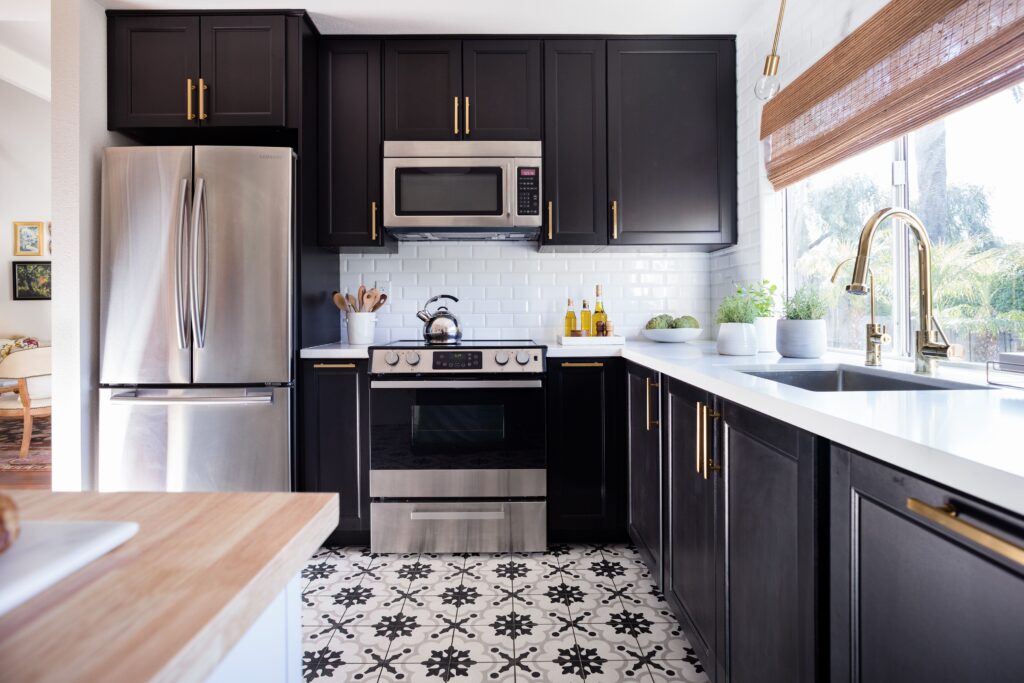 The Rise of Matte Finishes in Kitchen Remodeling 4 Stylish kitchen with black cabinets, gold hardware, patterned tile floor, white subway tile backsplash, and stainless steel appliances.