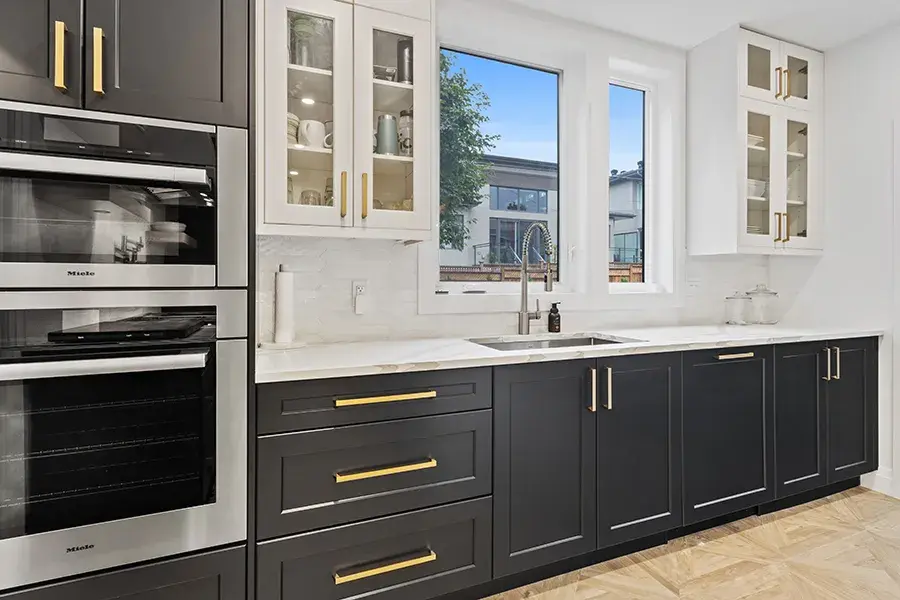  Elegant kitchen featuring dark lower cabinets with gold hardware and white upper cabinets with glass doors.