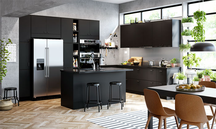  Black kitchen cabinets with a central island, modern appliances, wooden flooring, indoor plants, and large windows.